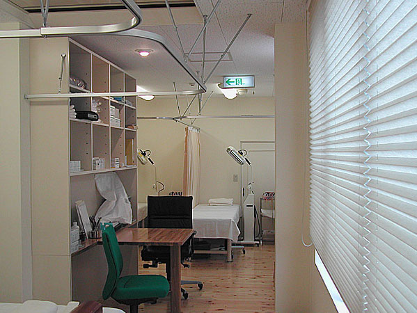 木造　M鍼灸院3、診察室中央に収納棚と机、手前と奥にカーテンで仕切られる治療ベッドがあります