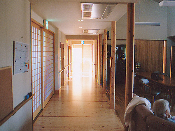 木造　三角グループホーム2、通路と居間は列柱で柔らかく区切り、玄関部分は明かりを通す障子で仕切ります、床のフローリングは材質と貼る向きを変えています